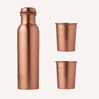 Image showcasing the Art of Vedas Copper Glass Bottle Set, featuring a 950ml copper bottle with a smooth, shiny finish and two complementary copper glasses, all arranged on a wooden table. The set reflects a warm, amber glow, emphasizing its elegant and traditional design suitable for health-focused hydration.