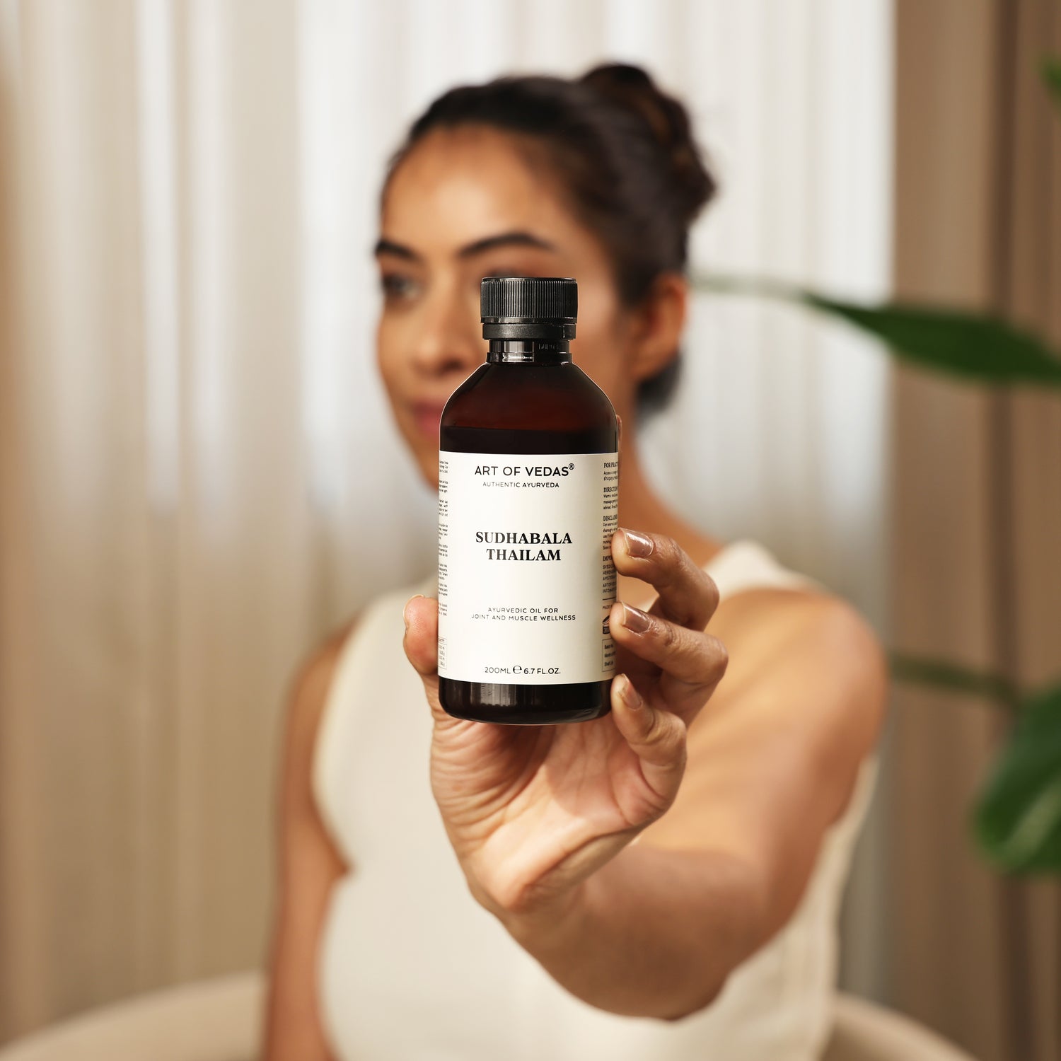 Art of Vedas Sudhabala Thailam - Woman Presenting Ayurvedic Oil Bottle for Bone Strength and Joint Health