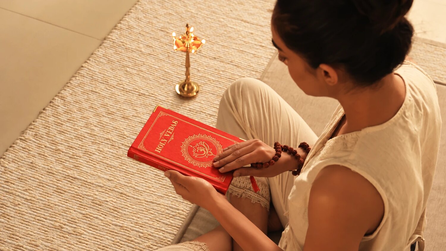 Woman seated on a woven mat reading the Holy Vedas beside a brass Ayurvedic lamp, for Art of Vedas